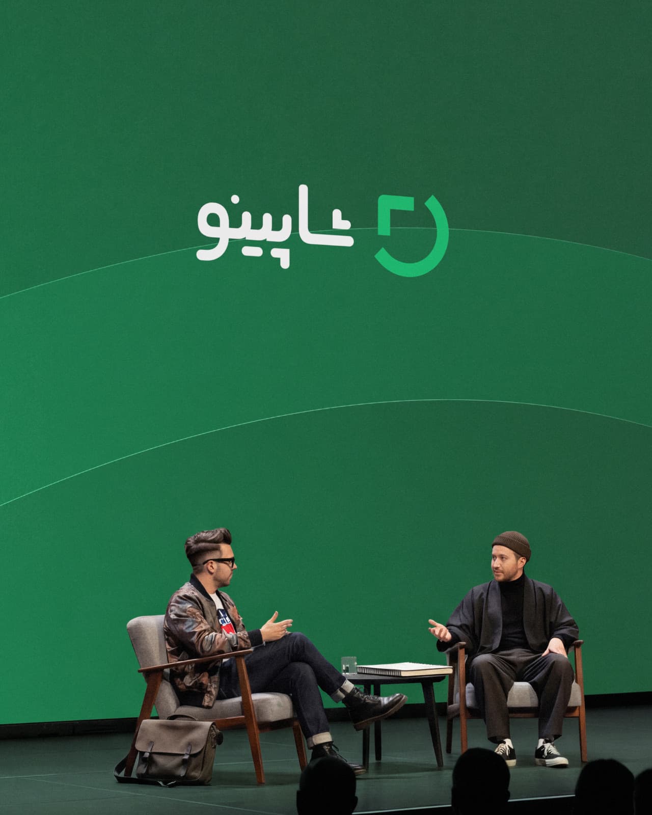 Two people in conversation on a stage, under a large green Shopino logo.